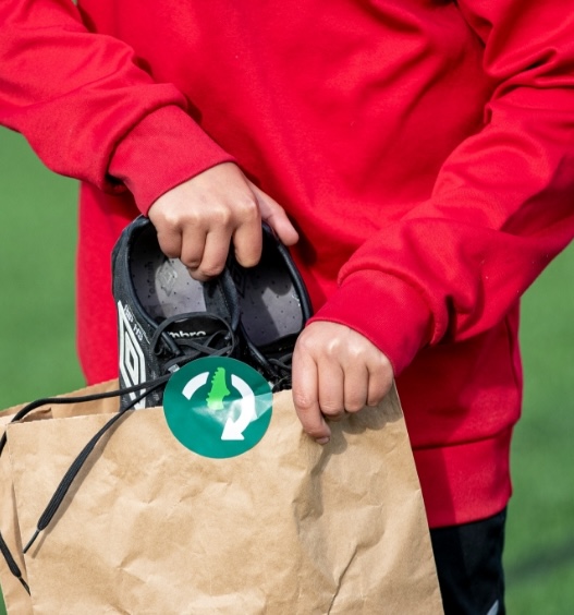 Person putting pre-loved football boots into a brown bag, helping reduce landfill waste with Utilita Football Rebooted.