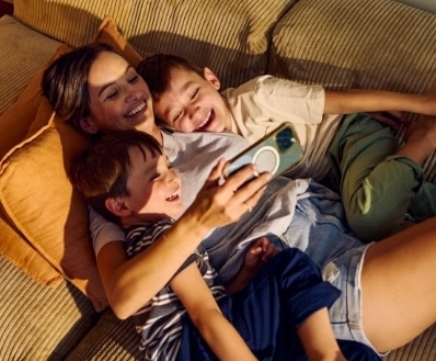 Mother and two sons laying on a sofa using a mobile phone to better understand and manage their household energy.